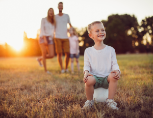 Family Image (3) Young boy sitting on a ball outdoors with family in the background.